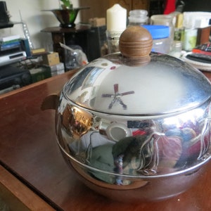 May include: A silver penguin-shaped ice cream maker with a wooden handle. The lid is open and reflects the surrounding environment.