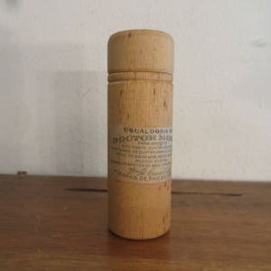 May include: A wooden container with a label that reads "USUAL DOSIS DOCTOR MOR PARA ADULTOS DOS HASTA QUATRO ANING DE QUATRO MESTE HIOS DE EDAD WAMEK SASE DERRETER EN AGUA PO PILDORA ENTERA PILDORAS DE RAICES"
