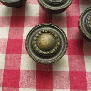 May include: Four antique brass cabinet knobs with a decorative, ornate design. The knobs have a raised, circular center and a textured, ring-like border.