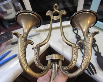 May include: A vintage brass candle holder with two sconces. The candle holder has an ornate design with curved arms and decorative leaf-like accents. The sconces are circular and have a slightly flared shape.