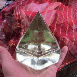 May include: A clear glass pyramid with a square base. The pyramid is made of faceted glass and reflects light.