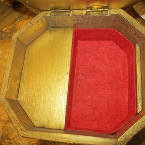 May include: A wooden jewellery box with a hinged lid and a red velvet interior. The box is octagonal in shape and has a gold finish.