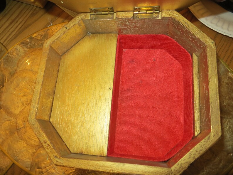 May include: A wooden jewellery box with a hinged lid and a red velvet interior. The box is octagonal in shape and has a gold finish.