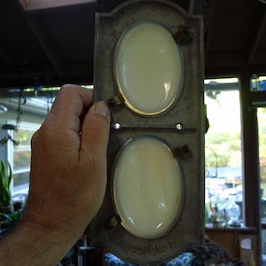 May include: A rectangular metal wall plate with a weathered gray finish featuring two vertically aligned oval-shaped off-white glass inserts. The metal frame has small mounting holes and the embossed text 1802-SA-2 at the bottom edge.