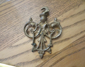 May include: Ornate gold metal hook with a decorative scroll design. The hook is designed to hang items from a ceiling or wall.