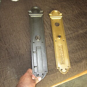 May include: Two antique door plates, one black and one gold, with ornate detailing. The gold plate has the word "LETTERS" engraved. Both plates have a keyhole and other hardware features, showcasing a vintage aesthetic.