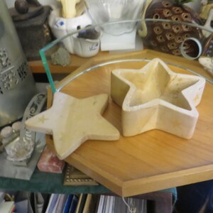 May include: Two wooden star-shaped boxes, one slightly larger than the other, are displayed on a wooden tray. The boxes are a light beige color and have a smooth, slightly textured surface.