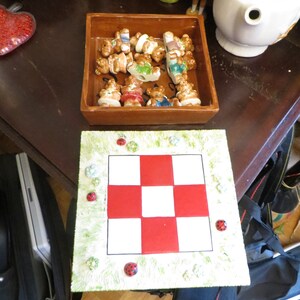 May include: A brown ceramic tray with a checkered design and a white border. The tray is filled with small ceramic figurines of bears wearing different colored clothes. The tray is sitting on a wooden table with a white teapot and other decorative items.