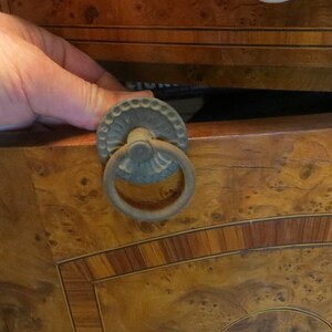 May include: A wooden drawer with a decorative brass ring pull. The drawer is made of wood with a burl veneer and has a dark brown stain. The drawer is open and the inside is visible.