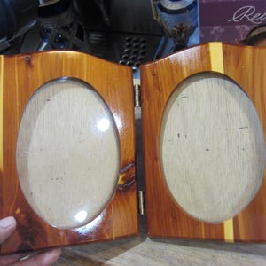 May include: A wooden picture frame with two oval openings. The frame is made of cedar wood and has a natural finish. The frame is hinged in the middle and can be folded closed.