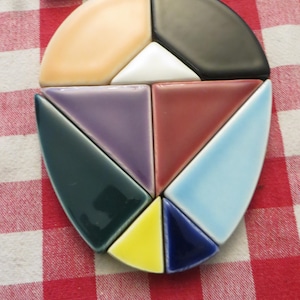 May include: A ceramic tile mosaic in the shape of a heart, made up of 10 individual tiles in various colors, including peach, black, white, purple, red, green, yellow, and blue.