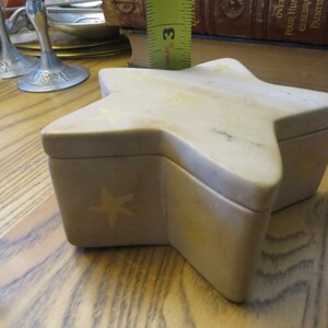 May include: A beige star-shaped trinket box with a five-pointed star design on the front. The box is made of a light-colored stone.