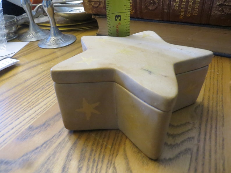 May include: A beige star-shaped trinket box with a five-pointed star design on the front. The box is made of a light-colored stone.