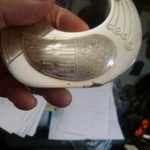 May include: A decorative bird-shaped object with a silver and white design. The bird has detailed wing and tail patterns, with a curved neck and a series of circular accents. The object appears to be made of metal and has a vintage aesthetic.