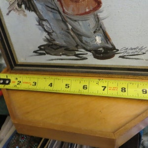 May include: A framed painting of a person in a red and white outfit, with a yellow measuring tape showing the frame is 9 inches wide.