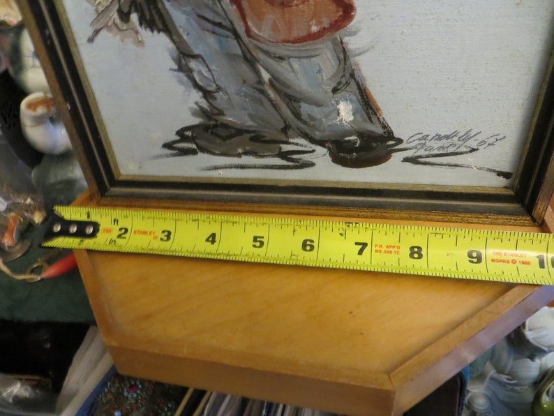 May include: A framed painting of a person in a red and white outfit, with a yellow measuring tape showing the frame is 9 inches wide.