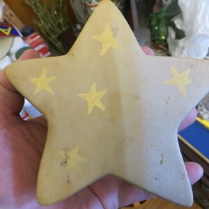 May include: A beige ceramic star with five points, decorated with five yellow stars. The star is slightly textured and has a rustic look.