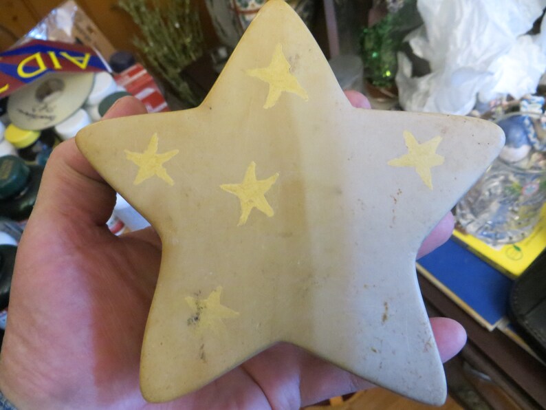 May include: A beige ceramic star with five points, decorated with five yellow stars. The star is slightly textured and has a rustic look.