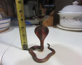 May include: A vintage cobra-shaped candle holder, primarily red with brass accents. The candle holder is approximately 5 inches tall. The cobra's head forms the candle cup, and the body coils along the base. The candle holder has a distressed finish.