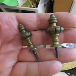 May include: Two gold-toned metal finials with a decorative design and a threaded screw base.