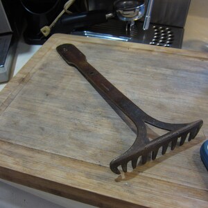May include: A rusty metal rake with a wooden handle. The rake is lying on a wooden cutting board.