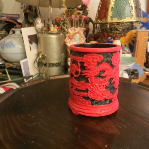 May include: A red and black Chinese style pen holder with a dragon design. The pen holder is made of lacquered wood and has a glossy finish.