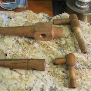 May include: Three wooden spigots, two with a 90-degree bend and one straight, are arranged on a light brown and gray speckled surface.