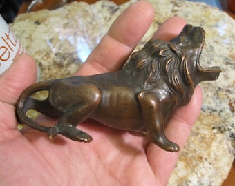 May include: A bronze lion figurine with a detailed mane and open mouth. The lion is standing on all fours and has a curled tail.