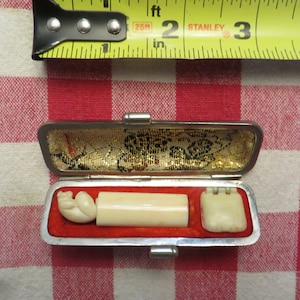 May include: A silver and red case with a white ivory stamp inside. The stamp has a carved animal figure on one end and a rectangular design on the other end.