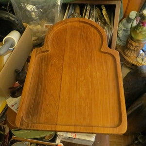 May include: A large, rectangular wooden serving board with a raised edge and a rounded arch at the top. The board is made of light brown wood with a natural grain pattern.