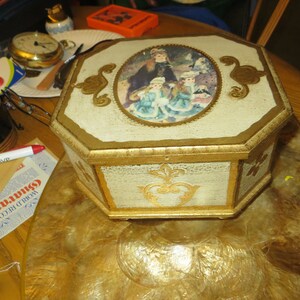 May include: Octagonal wooden box with a gold trim and a painted scene of three girls in a park. The box has a white background with gold accents.