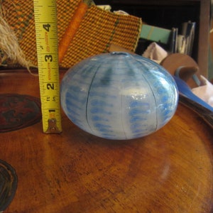 May include: A blue and white glass paperweight with a textured surface. The paperweight is round and has a white background with blue swirls and lines.