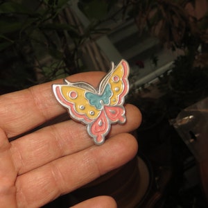 May include: A silver butterfly brooch with yellow, pink, and blue enamel accents.