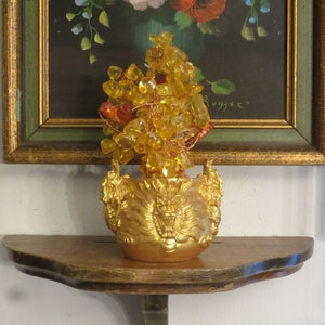 May include: A golden dragon-shaped pot with a yellow crystal tree inside. The pot is sitting on a wooden shelf in front of a framed painting.
