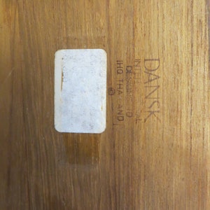 May include: A close-up of a wooden surface with a white label and the text "DANSK  DESIGN  IN  DENMARK  IHQ  THA  (C)"