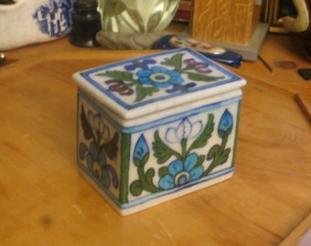 May include: A small, white, rectangular box with a hinged lid. The box is decorated with a blue, green, and white floral pattern. The box is made of ceramic and has a glossy finish.