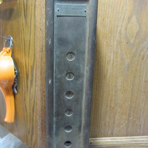 May include: An antique elevator control panel with buttons for floors 1 through 5. The panel is made of a dark metal with a rectangular shape and a small plaque at the top. The panel is mounted on a wooden surface.