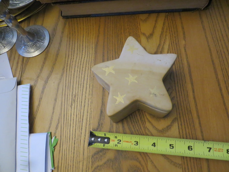 May include: A beige star-shaped trinket box with gold stars painted on it. The box is sitting on a wooden surface.