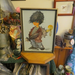 May include: A framed painting of a cartoon character with black hair, blue eyes, and a brown jacket. The character is holding a yellow object in their right hand. The painting is set on a wooden shelf.