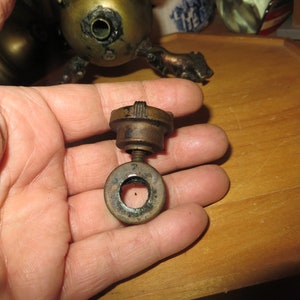 May include: A close-up of a brass lamp part with a threaded ring and a screw. The part is held in a hand.