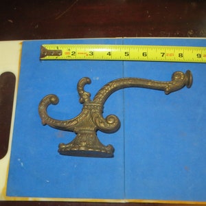 May include: A gold-toned metal hook with an ornate design. The hook is about 7 inches long and has a decorative base.