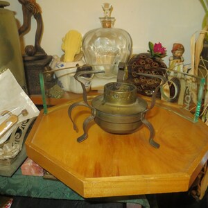 May include: A brass burner with four legs sits on a wooden octagonal tray. The burner is on a glass surface with other decorative items.