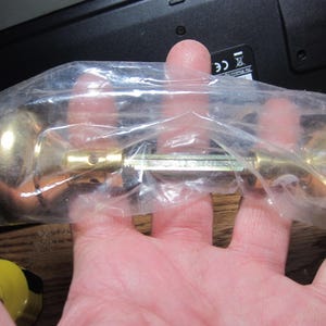 May include: A pair of gold door knobs in a clear plastic bag. The knobs are round and have a smooth finish.