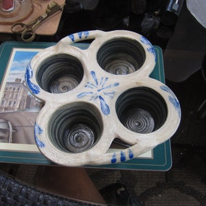 May include: A white ceramic baking dish with four individual round molds. The dish has a blue and white floral design and a handle on the side.