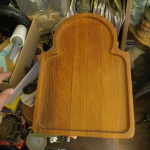 May include: A rectangular wooden cutting board with a rounded arch at the top. The board is made of light brown wood and has a smooth surface.