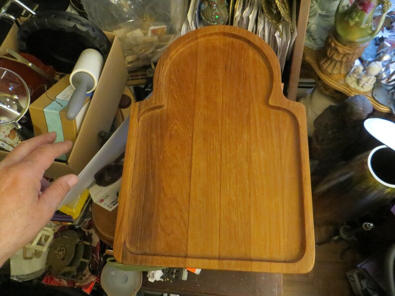 May include: A rectangular wooden cutting board with a rounded arch at the top. The board is made of light brown wood and has a smooth surface.