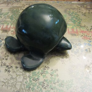 May include: A dark green ceramic turtle figurine with a smooth, glossy finish. The turtle is in a walking position with its head and legs extended.