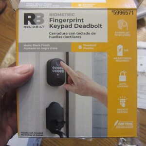 May include: A matte black finish Reliabilt Biometric Fingerprint Keypad Deadbolt. The box shows the keypad and deadbolt, with a finger touching the keypad. Features include auto-locking and a backlit keypad. Stores up to 50 users.