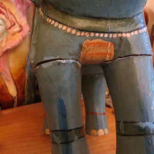 Puede incluir: Una figurita de elefante de madera pintada en tonos azules y verdes con detalles blancos. El elefante tiene un acabado de pintura desgastado y le falta un peque&ntilde;o trozo de pintura en el lateral.