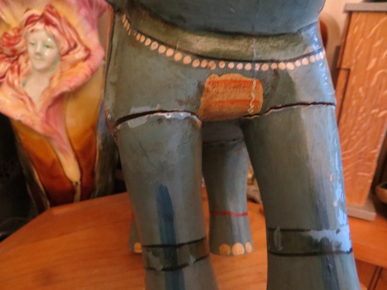 Puede incluir: Una figurita de elefante de madera pintada en tonos azules y verdes con detalles blancos. El elefante tiene un acabado de pintura desgastado y le falta un peque&ntilde;o trozo de pintura en el lateral.